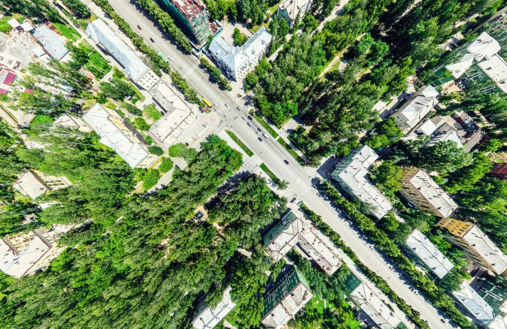 Aerial city view with crossroads and roads, houses, buildings, parks and parking lots. Sunny summer panoramic image